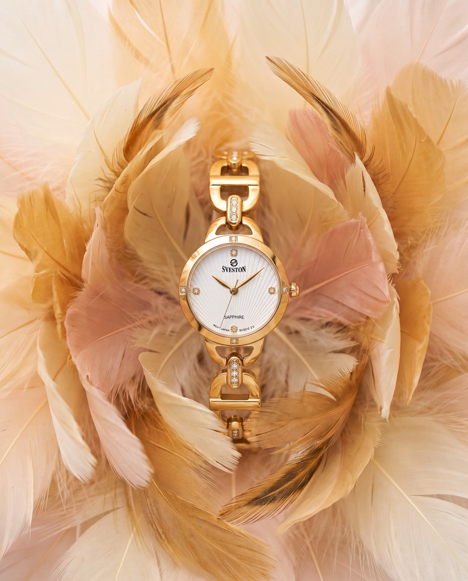 Delicate gold Sveston women's watch surrounded by soft blush and champagne feathers